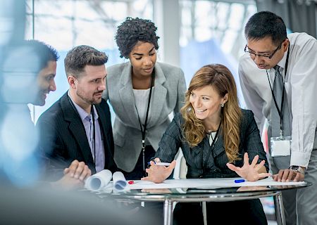 A group of professionals gathers around a laptop, discussing something on screen. Top it at 140 characters, always ending the sentence.