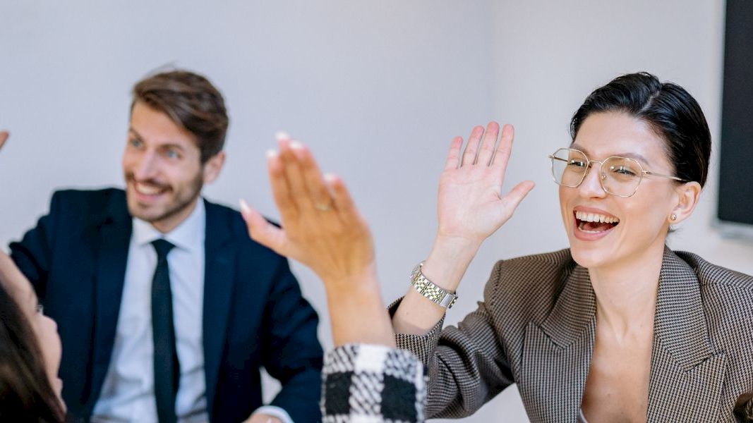 A diverse group of professionals in a meeting celebrate with high-fives and smiles, indicating teamwork and success.