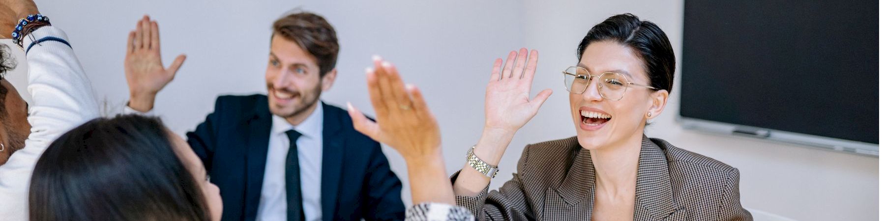 A diverse group of professionals in a meeting celebrate with high-fives and smiles, indicating teamwork and success.