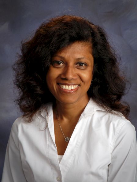 A smiling woman with shoulder-length dark hair wearing a white blouse, posing for a professional portrait.