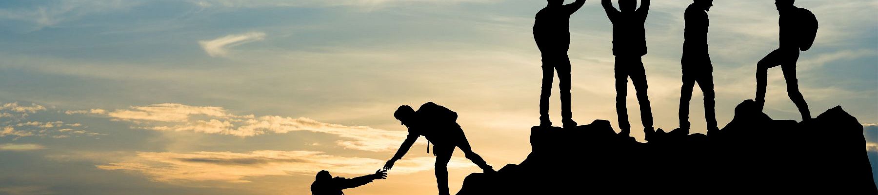 Silhouetted group of friends cheering and celebrating atop a hill at sunset, raising hands against a glowing sky.