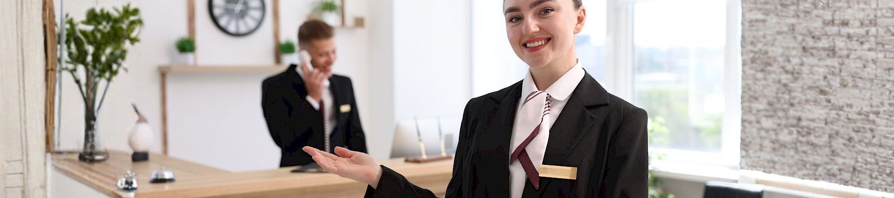 A smiling receptionist in a suit welcomes guests at the office front desk.