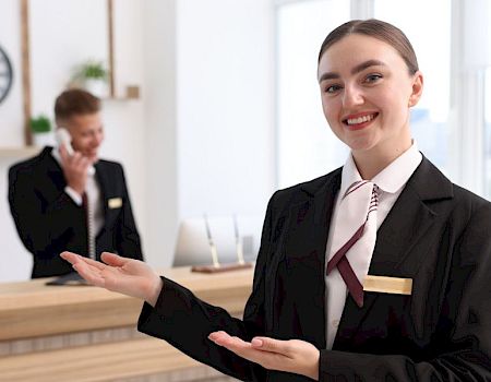 A smiling receptionist in a suit welcomes guests at the office front desk.